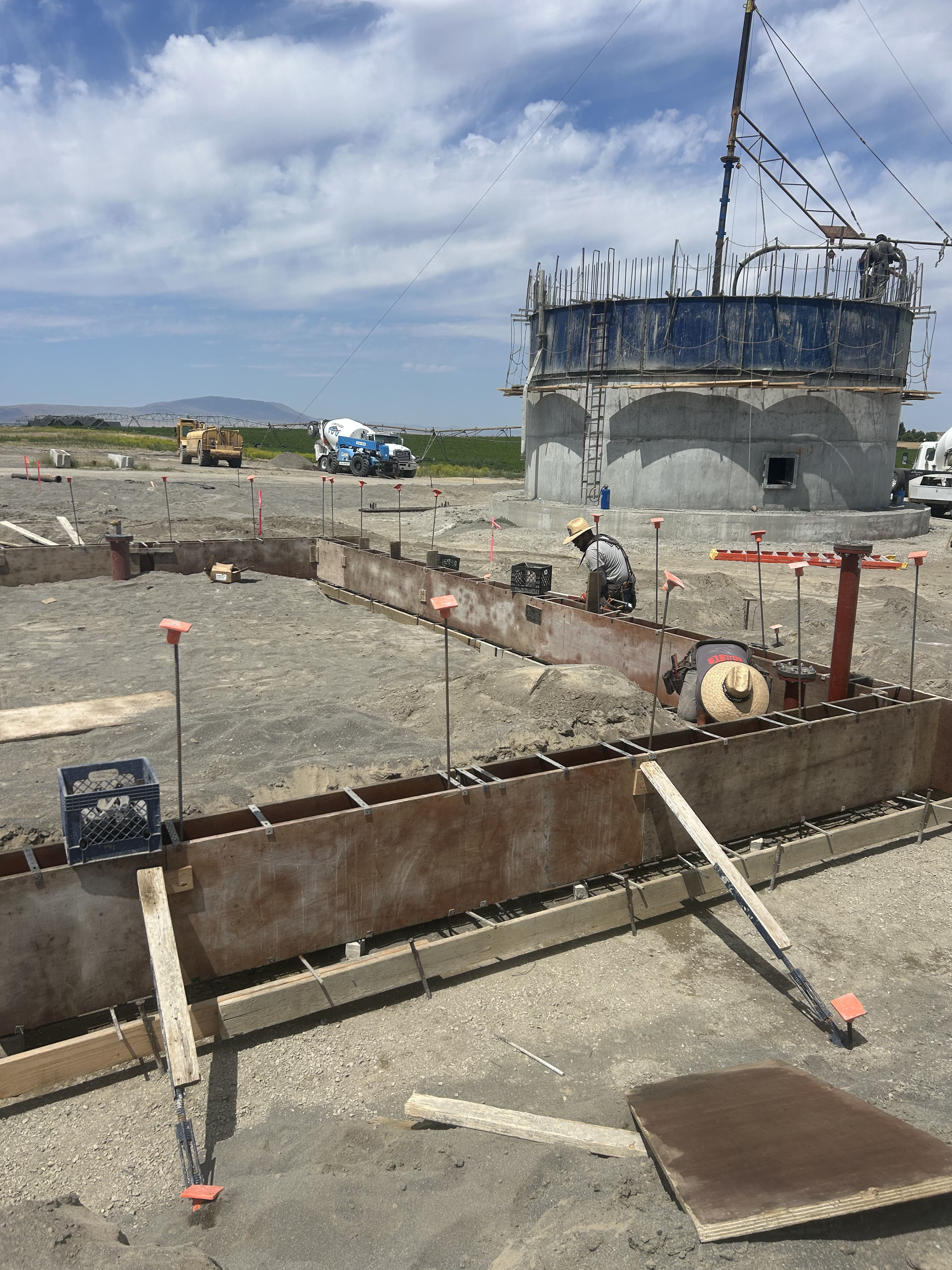 Concrete tank construction with rebar forming in foreground and cement mixer in background