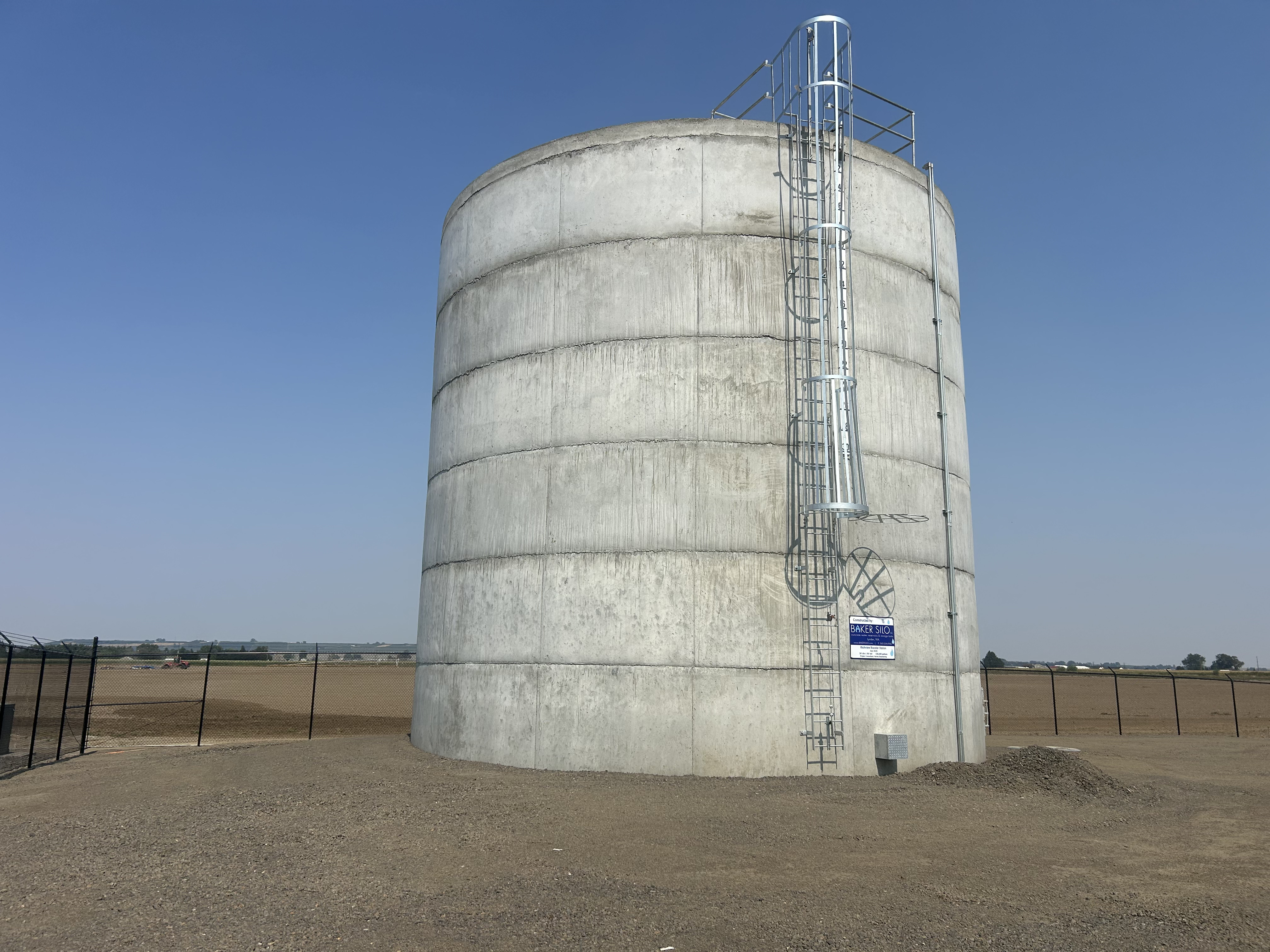 Completed concrete water treatment storage tank with metal access ladder against blue sky